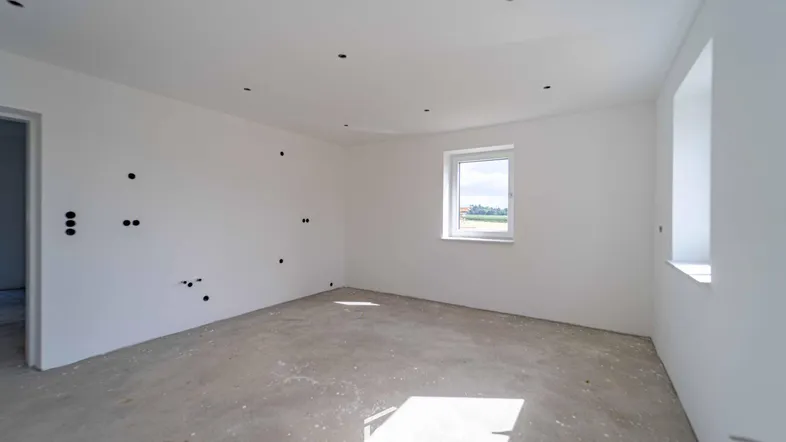 Unfertiger Innenraum mit weißen Wänden und Betonboden, bereit für den weiteren Ausbau.