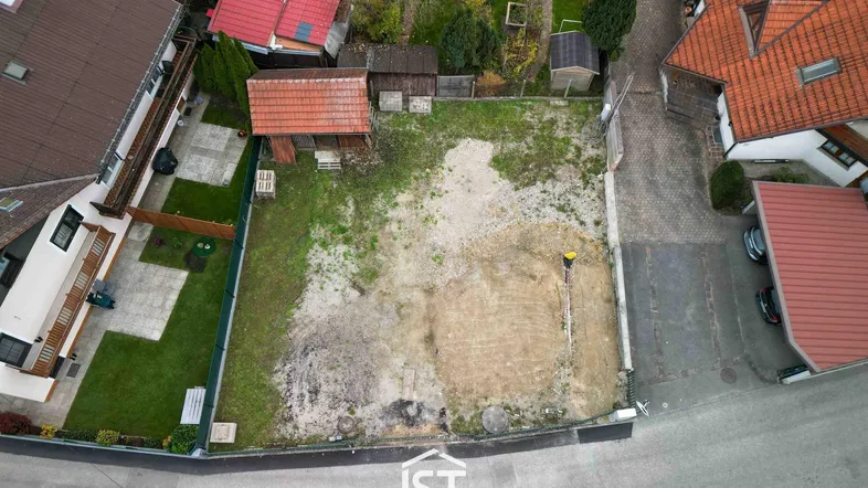 Luftaufnahme eines unbebauten Grundstücks mit umliegenden Wohnhäusern, Gärten und einem kleinen Schuppen.