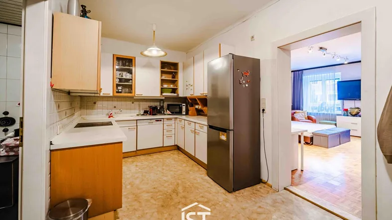 Küche mit älteren Einbaumöbeln, Kühlschrank und Zugang zu einem weiteren Raum.