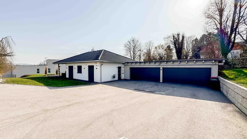 Modernes Einfamilienhaus mit großem Vorplatz, Doppelgarage und gepflegtem Rasen unter blauem Himmel.