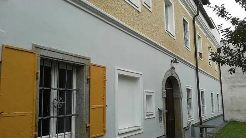 Historisches Gebäude mit gelber und hellblauer Fassade, Fensterläden und einem gewölbten Eingangsbereich.