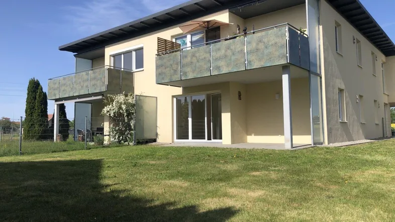 Modernes Mehrfamilienhaus mit Balkonen und Grünfläche unter blauem Himmel.