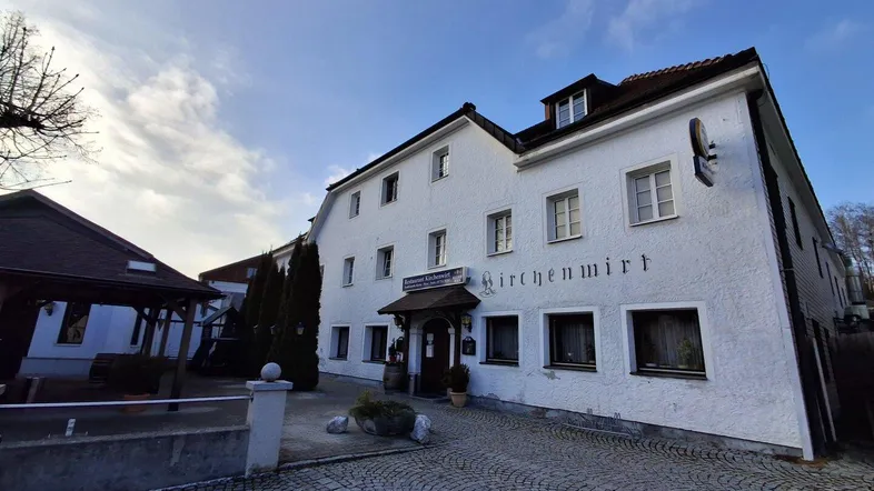 Weißes Gebäude mit traditioneller Architektur, gepflastertem Vorplatz und blauem Himmel.