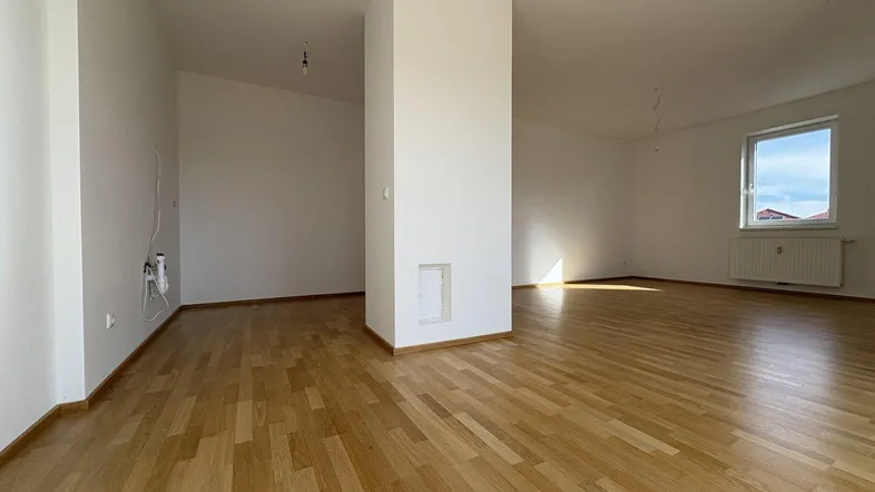 Helles, leeres Wohnzimmer mit Parkettboden und einem zentralen Pfeiler, bereit zur individuellen Gestaltung.