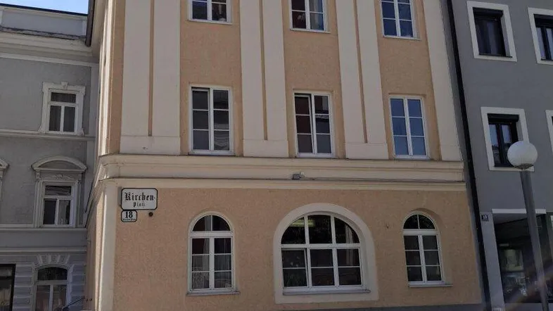 Ansicht eines traditionellen Gebäudes mit beiger Fassade, mehreren Fenstern und Rundbogenfenstern im Erdgeschoss.