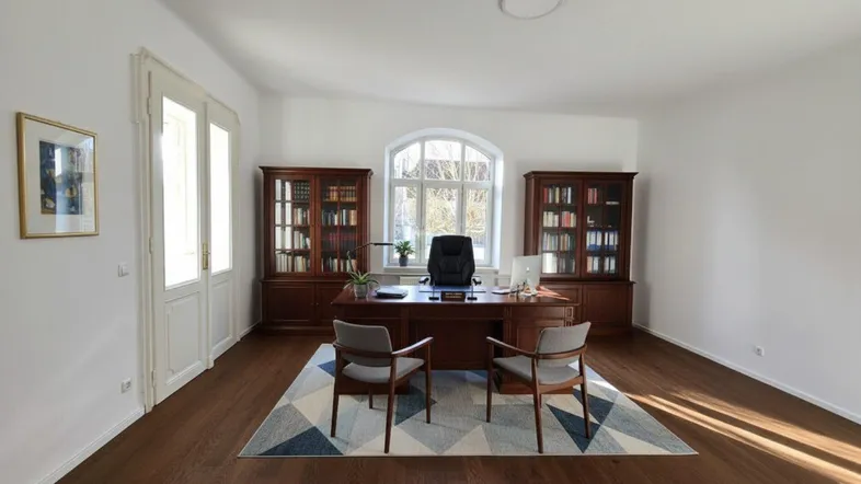 Geräumiges Büro mit klassischem Holzschreibtisch, Bücherregalen und großen Fenstern, das viel Tageslicht hereinlässt.