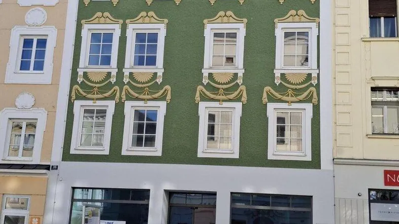 Historisches Gebäude mit auffälliger grüner Fassade und traditionellen Verzierungen in einer städtischen Umgebung.