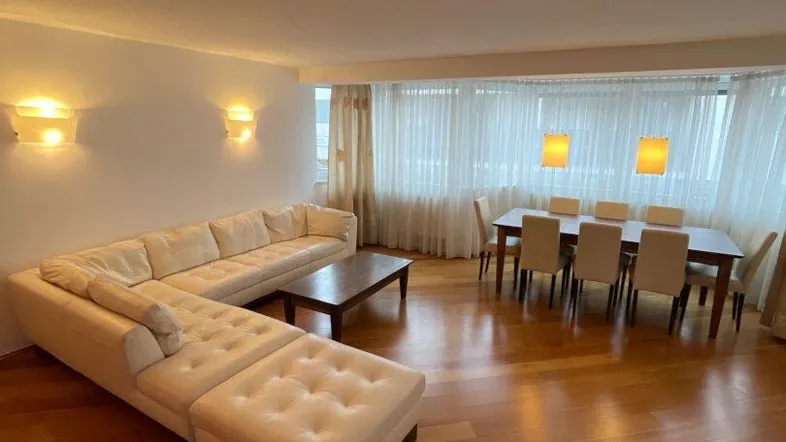 Geräumiger Wohn-Essbereich mit beigem Sofa, Parkettboden und viel Tageslicht durch die großen Fenster.