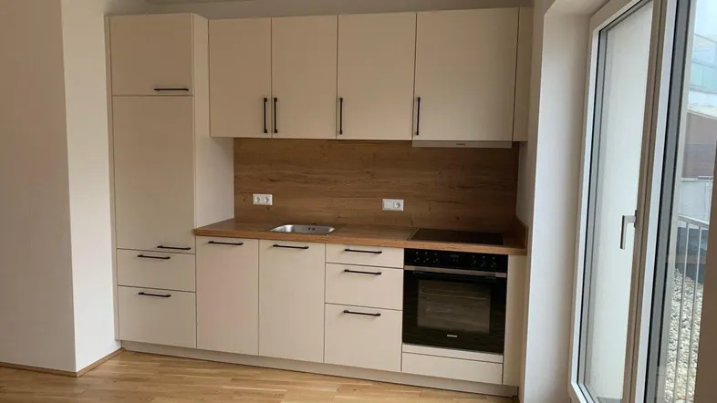 Moderne Einbauküche in hellem Beige mit Holzoptik-Arbeitsplatte und integrierten Geräten.