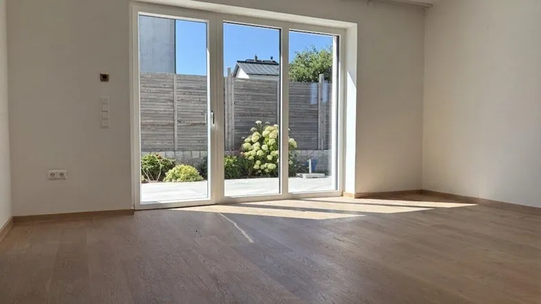 Helles Wohnzimmer mit Holzboden und großen Fenstern, die Zugang zu einer Terrasse bieten.
