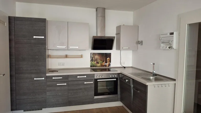 Moderne L-förmige Einbauküche mit grauen und weißen Schränken, integrierten Geräten und Laminatboden.