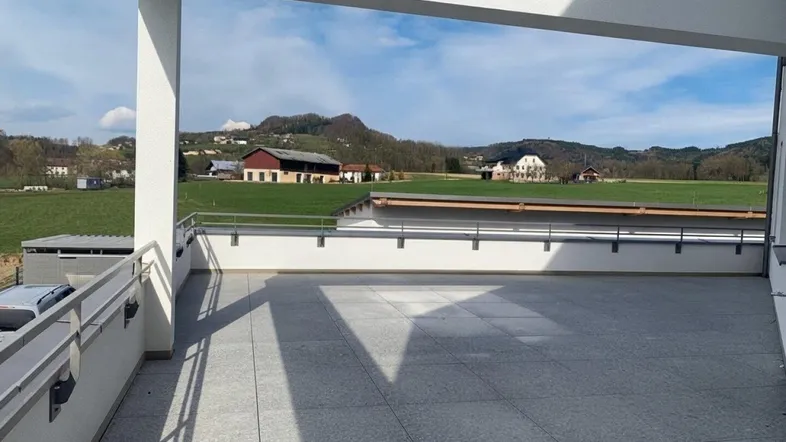 Geräumige Terrasse mit Fliesenboden und weitem Blick über grüne Felder und die umliegende Landschaft.