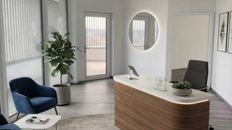 Moderner Empfangsbereich mit Holztresen, blauen Sesseln und Zugang zu einer Terrasse.
