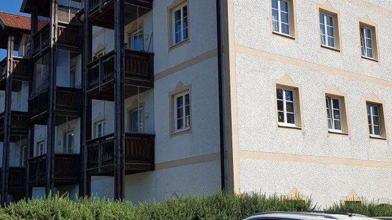 Mehrstöckiges Gebäude mit Balkonen und geparkten Autos davor unter blauem Himmel.
