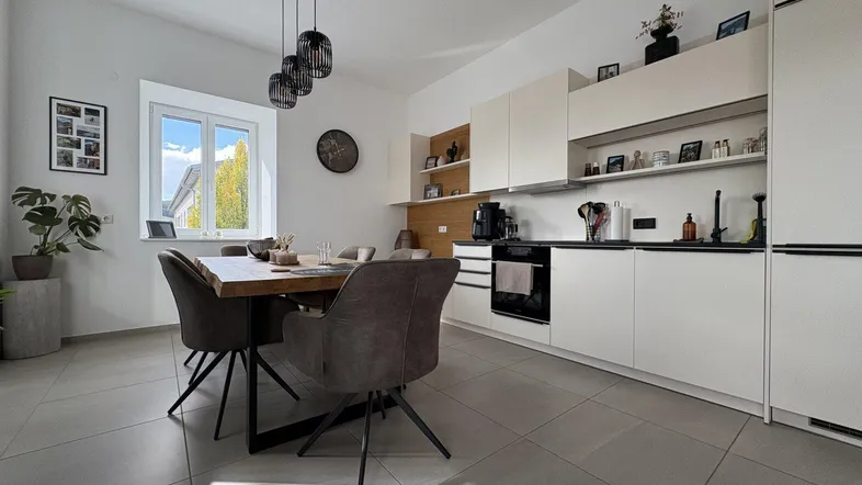 Moderne offene Küche mit Essbereich, weißen Schränken, Holzakzenten und Fliesenboden.