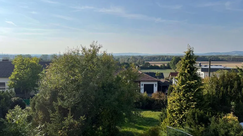 Weitläufiger Blick über die Landschaft mit Feldern, Bäumen und benachbarten Häusern unter blauem Himmel.