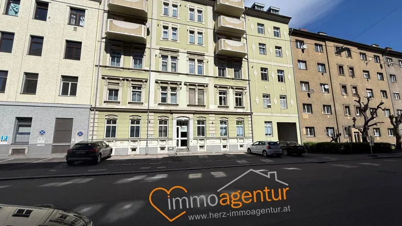 Mehrfamilienhaus mit klassischer Fassade und Balkonen an einer städtischen Straße.