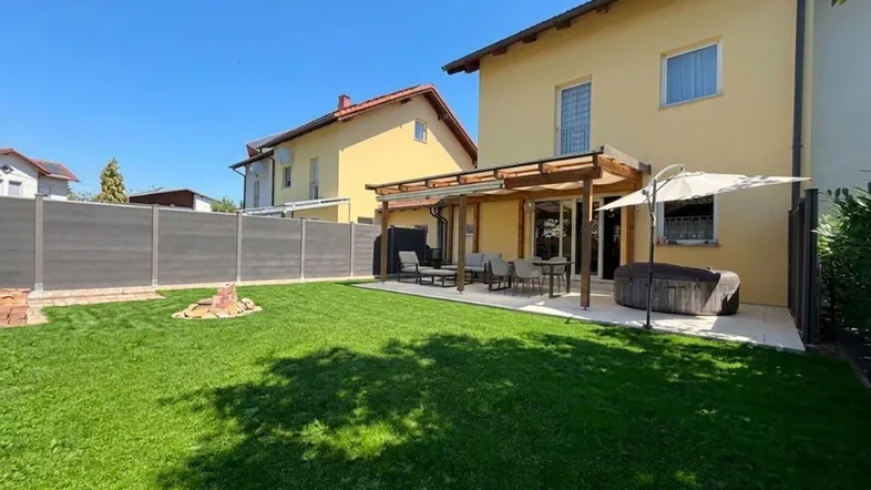 Großer, gepflegter Garten mit Rasenfläche, möblierter Terrasse und Holzpergola hinter dem Haus.