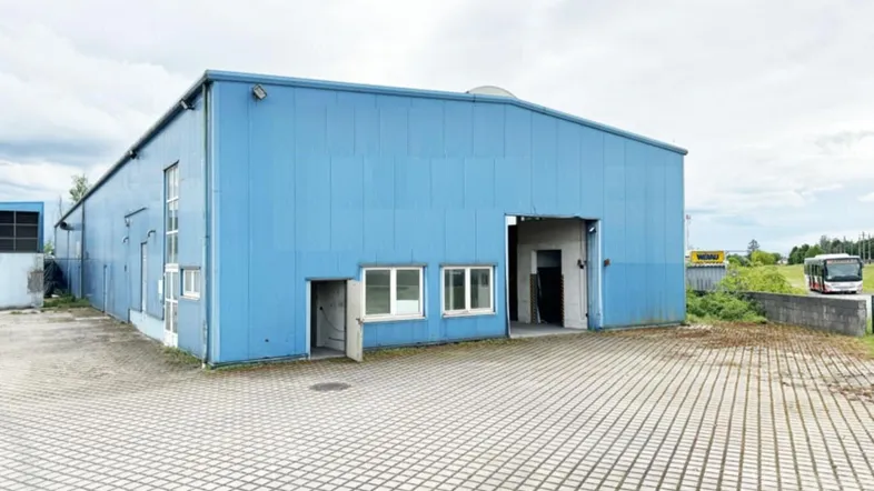Außenansicht eines großen blauen Industriegebäudes mit gepflastertem Vorplatz und Zufahrt.
