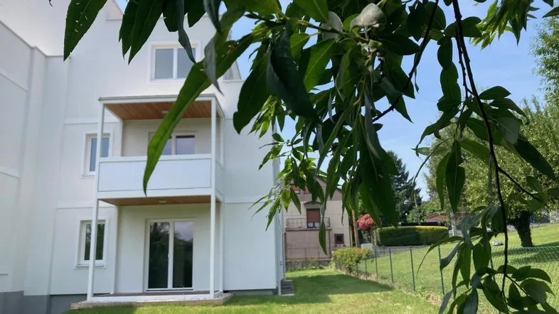 Weißes Mehrfamilienhaus mit Balkonen und direktem Zugang zum grünen Gartenbereich.