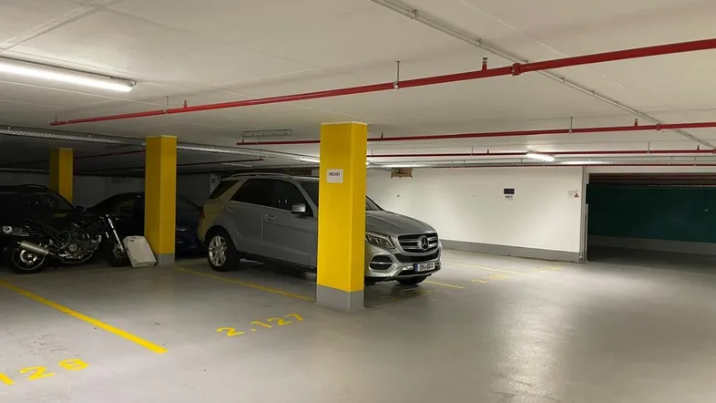 Tiefgarage mit markierten Stellplätzen, gelben Säulen und sichtbaren Brandschutzrohren an der Decke.