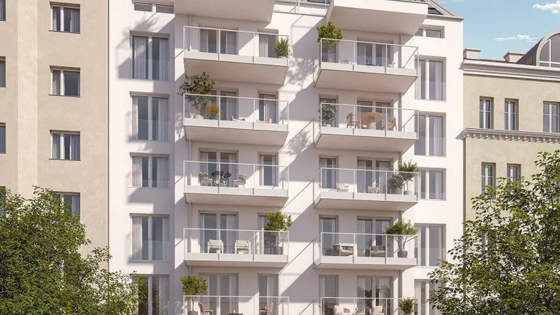 Moderne Wohnhausfassade mit zahlreichen Balkonen und großen Fenstern, umgeben von Bäumen und parkenden Autos.