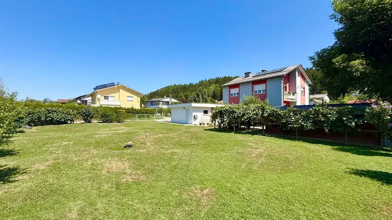 Großer, gepflegter Rasenbereich mit umliegenden Häusern und viel Grün unter blauem Himmel.