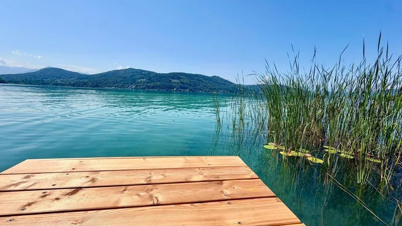 Holzsteg am Seeufer mit klarem türkisfarbenem Wasser und Blick auf die umliegenden Berge.