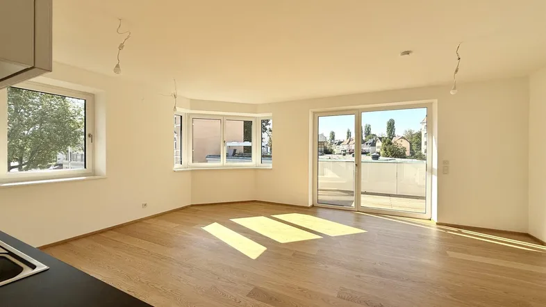 Helles Zimmer mit Holzboden, großen Fenstern und Zugang zu einem Balkon.