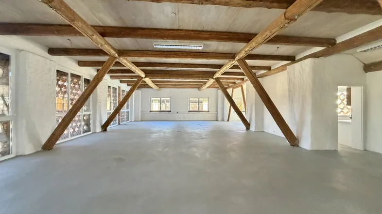 Großer, heller Raum mit freiliegenden Holzbalken und weiß getünchten Wänden, ideal für verschiedene Nutzungen.