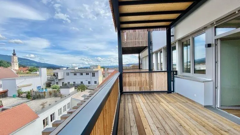 Geräumiger Balkon mit Holzboden und weitem Blick über die Stadt und die umliegenden Berge.