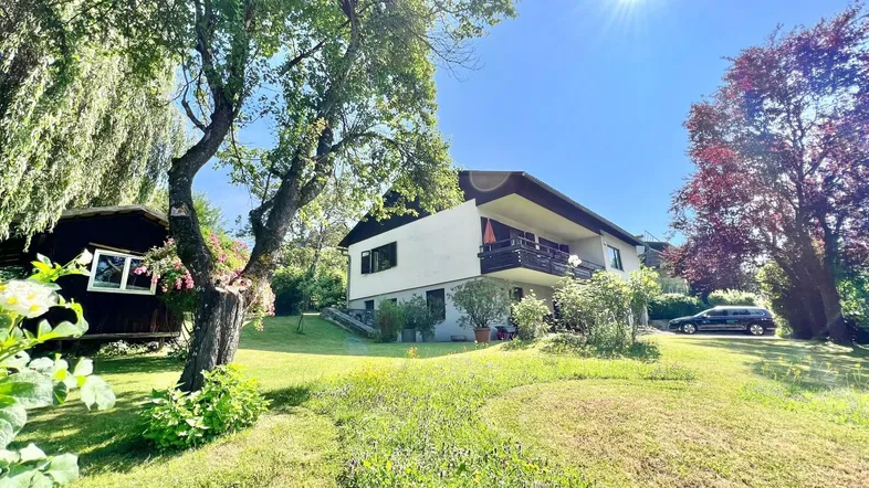 Haus mit großem Garten und altem Baumbestand unter strahlend blauem Himmel.