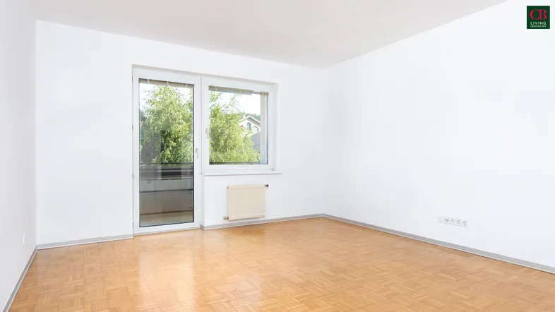 Helles, leeres Zimmer mit Parkettboden und Zugang zu einem Balkon.