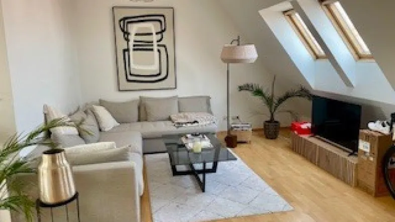 Helles Wohnzimmer im Dachgeschoss mit gemütlichem Sofa, Holzboden und Dachfenstern.