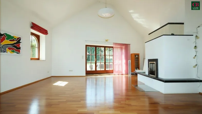Geräumiges Wohnzimmer mit Holzboden, Kamin und viel Tageslicht durch große Fenster und Terrassentür.