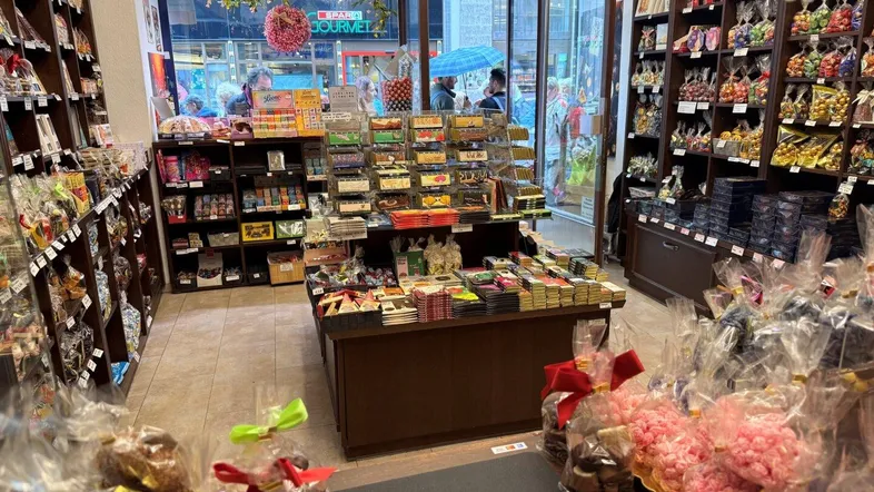 Innenansicht eines Süßwarengeschäfts mit reich gefüllten Regalen und Blick zur Straße durch große Fenster.