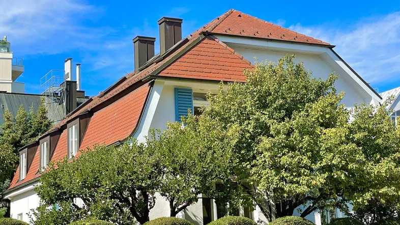 Elegante Stadtvilla mit markantem Mansarddach und gepflegter Gartenbepflanzung unter blauem Himmel.