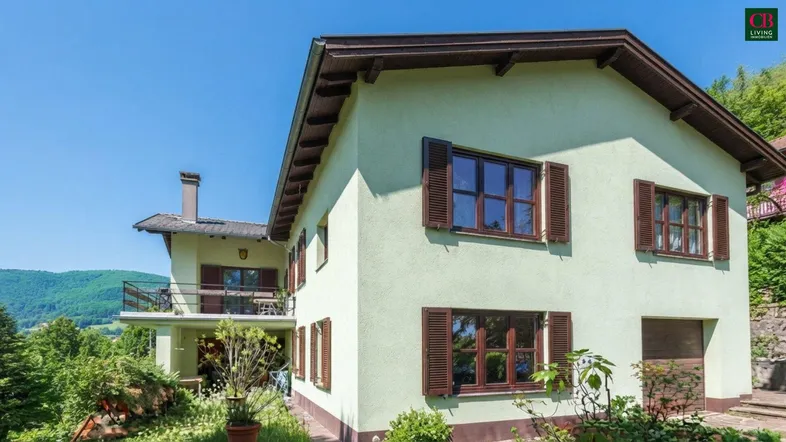 Grünes Haus mit braunen Fensterläden und Balkon in ländlicher Umgebung.