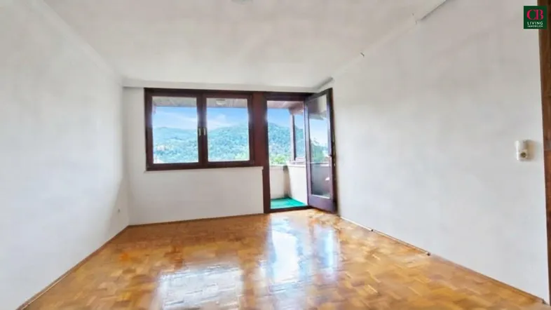 Helles Zimmer mit Parkettboden, weißen Wänden und Zugang zu einem kleinen Balkon mit Bergblick.