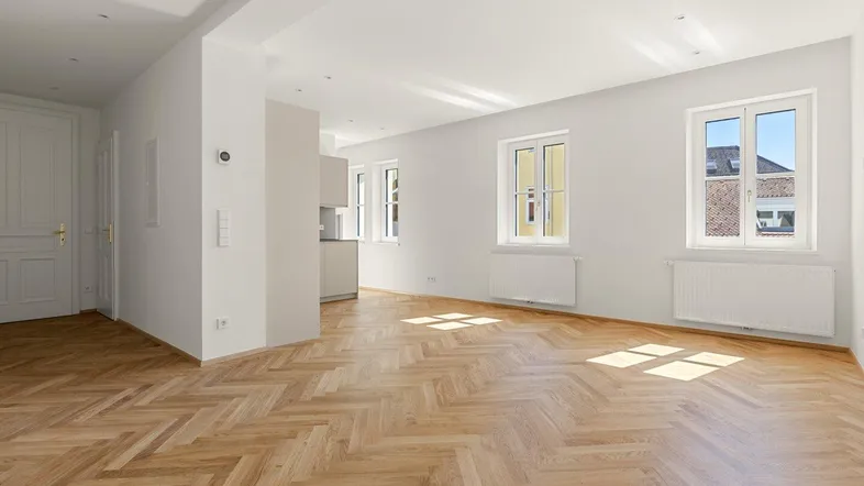 Helles Wohnzimmer mit Fischgrätparkett und großen Fenstern, das viel Tageslicht hereinlässt.
