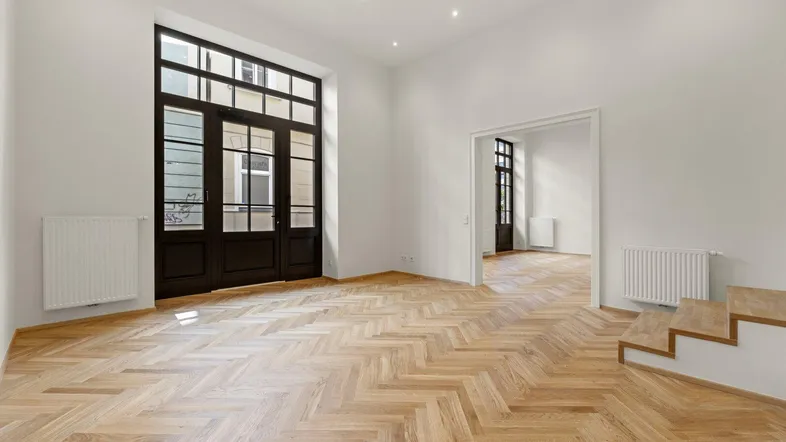 Geräumiges Wohnzimmer mit Fischgrätparkett, hohen Fenstern und viel natürlichem Licht, frisch renoviert.