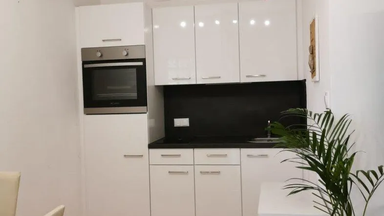 Moderne Küchenzeile mit weißen Hochglanzfronten, integriertem Backofen und hellem Holzfußboden.