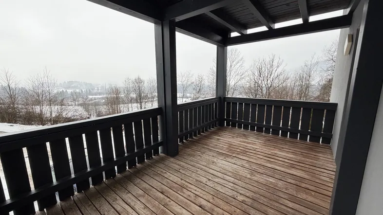 Überdachter Balkon mit Holzboden und Blick auf die verschneite Landschaft und Berge.