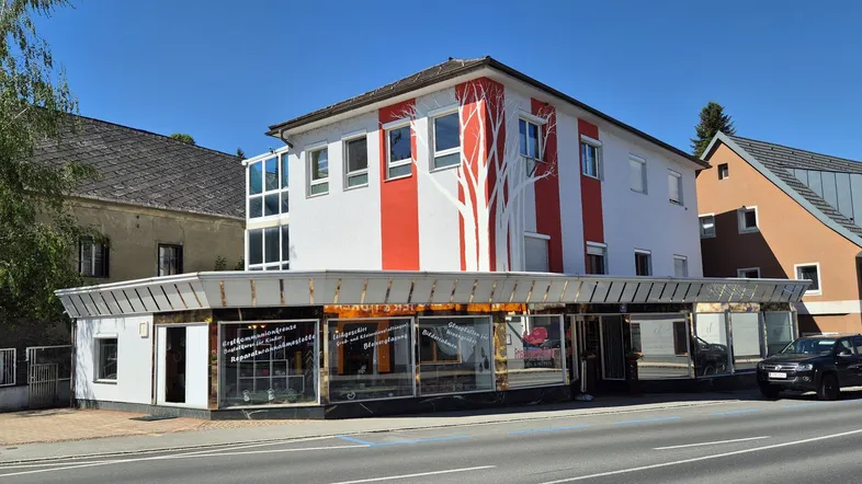 Gebäude mit weißer und roter Fassade, großen Schaufenstern und einem Baumdesign.