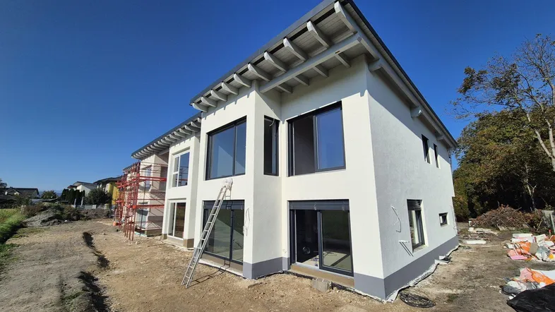 Neubauhaus in moderner Architektur mit großen Fenstern und Baustelle im Vordergrund.