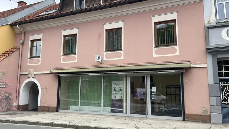 Historisches Gebäude mit rosafarbener Fassade, großen Schaufenstern im Erdgeschoss und Wohnungen darüber.