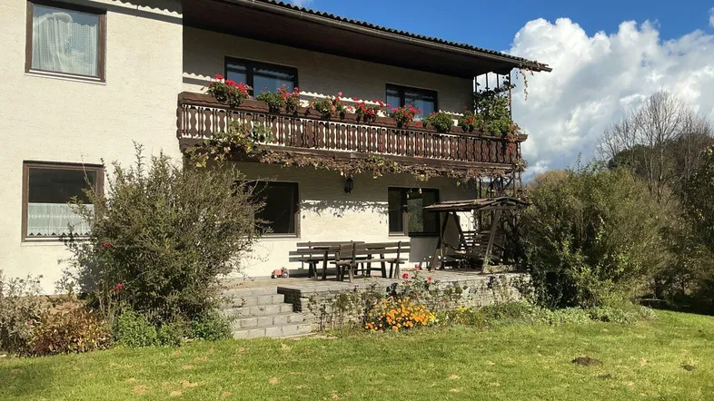 Traditionelles Haus mit Balkon, Terrasse und Gartenbereich unter blauem Himmel.