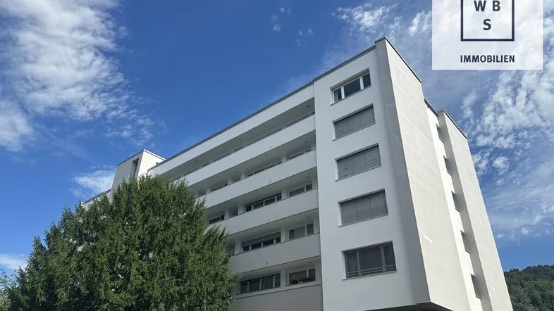 Modernes Mehrfamilienhaus mit weißer Fassade und mehreren Balkonen unter blauem Himmel.