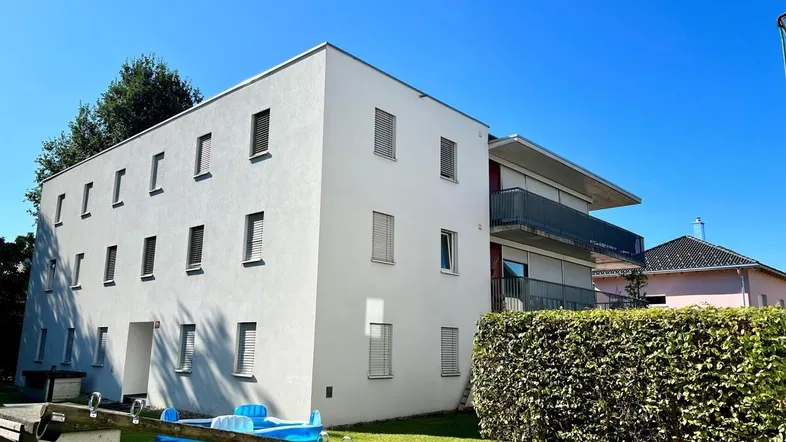 Modernes Mehrfamilienhaus mit weißer Fassade und kleinem Spielbereich im Vorgarten.