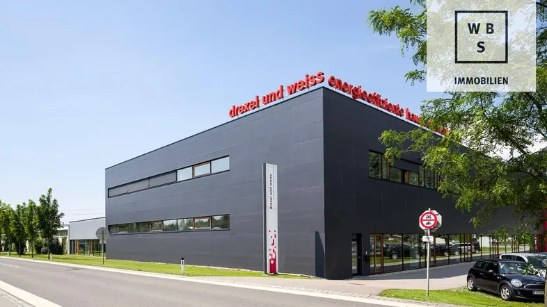 Modernes Geschäftsgebäude mit dunkler Fassade und roten Akzenten, umgeben von Bäumen und einer Straße.